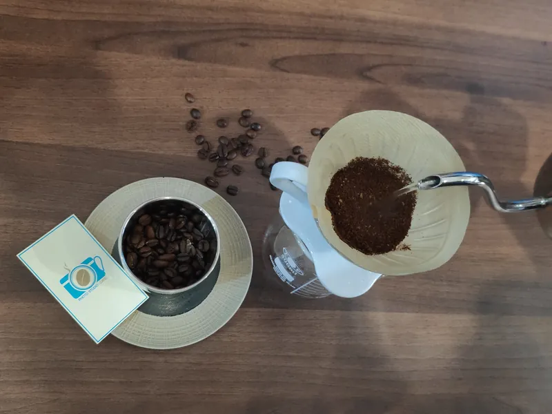伶 Kopi 的手沖咖啡：濾杯、手沖壺、一罐咖啡豆，旁邊是印著相機咖啡杯 Logo 的小卡