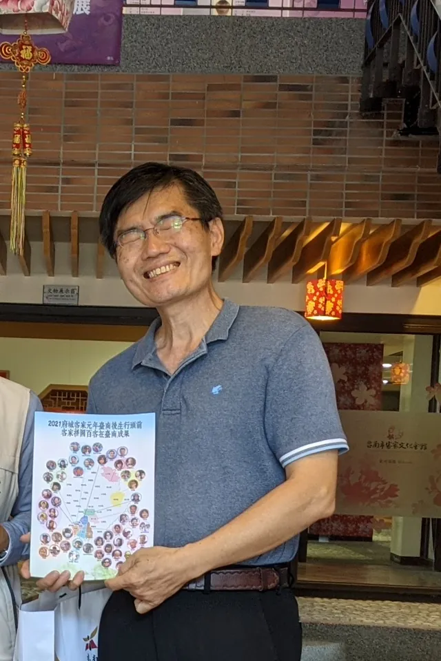 2021 年 12 月，老闆劉政中在臺南市客家文化會館，拿著收錄〈我的女兒〉的「客家拼圖・百客在臺南」成果書