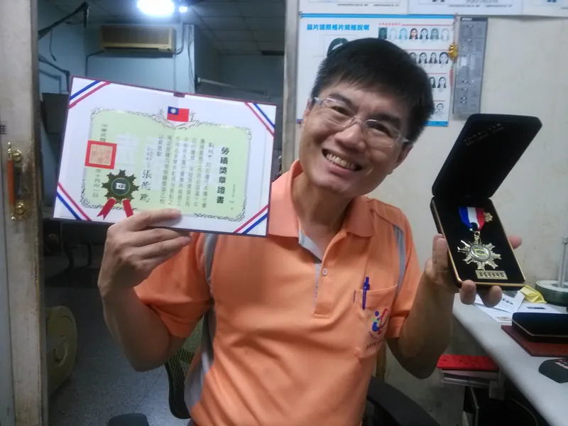 2016 年 10 月，老闆劉政中拿著救國團四等勞績獎章和證書，義務工作滿十年
