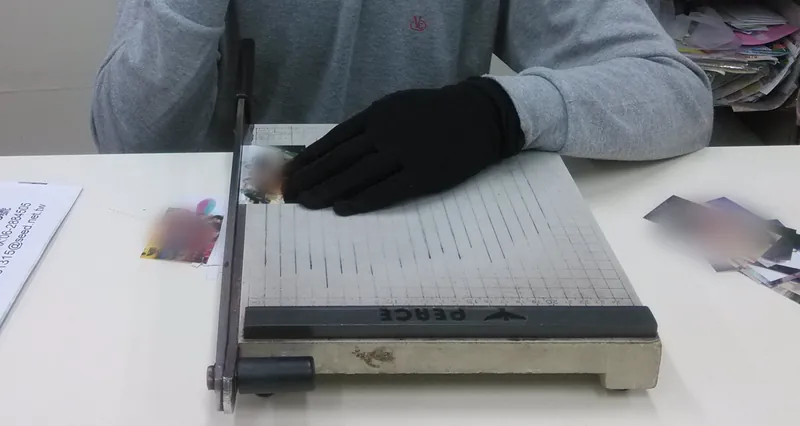 戴著黑手套，把洗好的照片放在裁紙台上一張一張裁